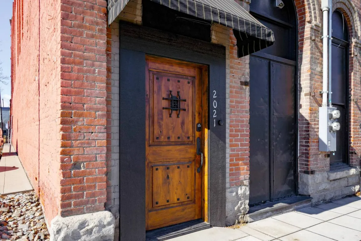 The historic exterior entrance to the West Empire Theatre Loft, featuring a decorative wooden door and classic brickwork. The number 2021 is prominently displayed, suggesting a sense of welcome and heritage. The inviting facade hints at the comfort waiting inside after a day on the mountain.