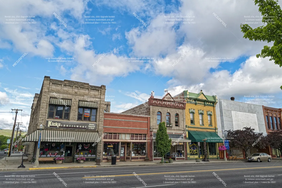A cheerful street scene featuring the storefronts of various shops, colorful awnings, and trees lining the sidewalk. The image conveys a sense of lively community with locals and visitors enjoying shopping and dining amidst a picturesque historic setting.