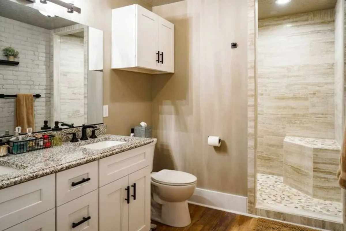 The bathroom is modern and stylish, featuring a granite countertop, a spacious walk-in shower with glass doors, and a well-lit mirror. The overall ambiance is serene, perfect for refreshing after a busy day.
