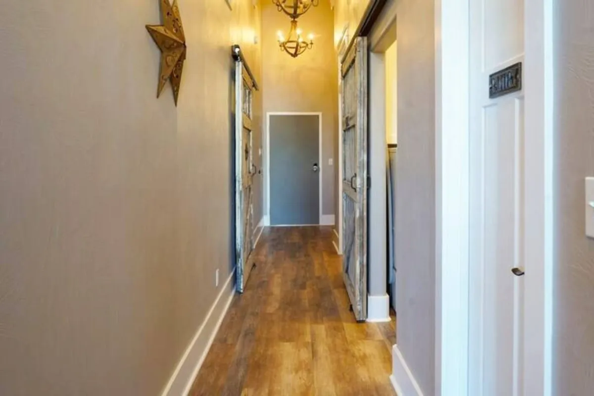 A warmly lit hallway with wooden flooring, hanging decorative star lights, and inviting sliding barn doors. The entryway features seasonal touches and evokes a sense of arrival and welcoming, suggesting the festive atmosphere experienced during local events.