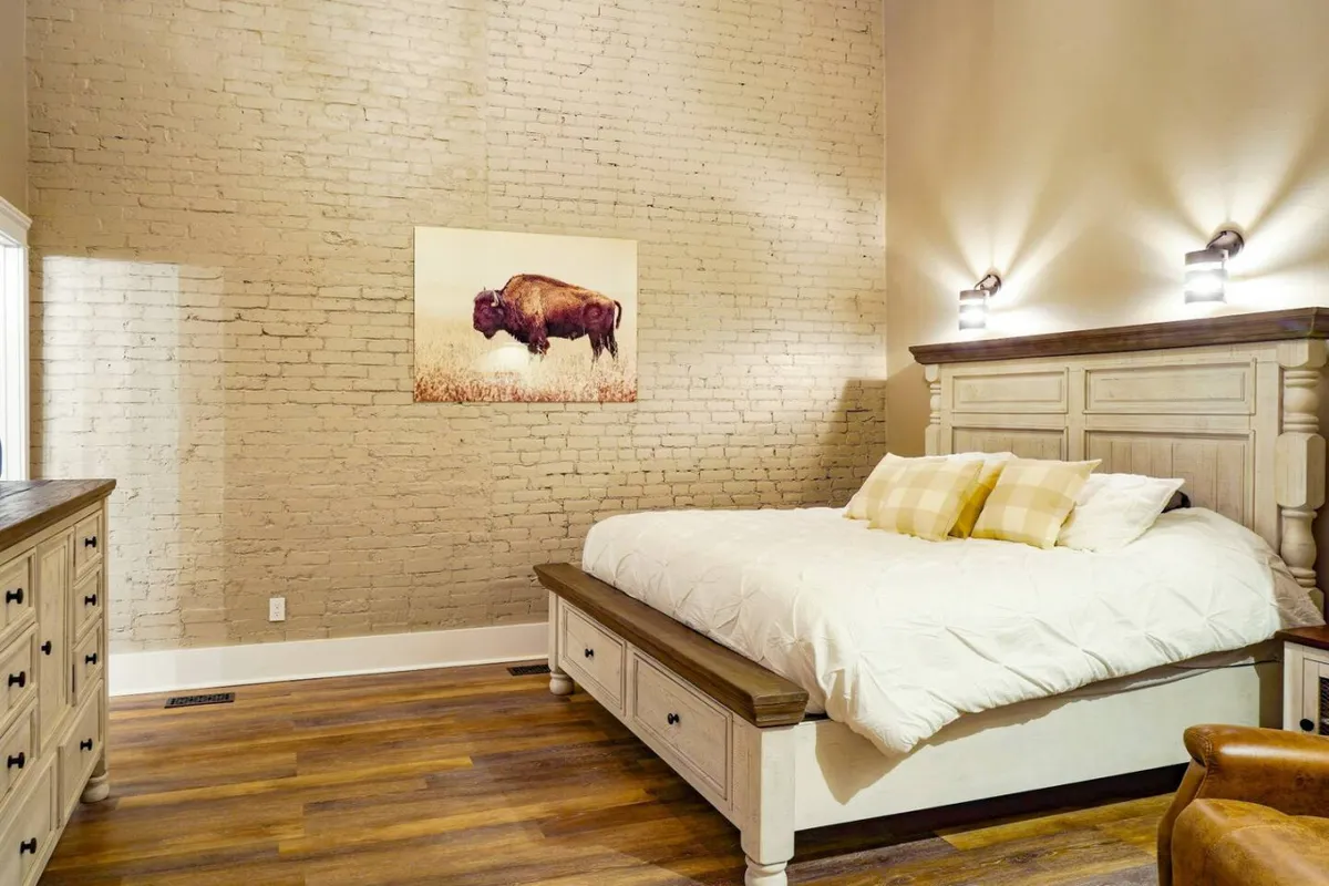 This image highlights the main bedroom, showcasing a plush king bed adorned with inviting bedding and a striking buffalo artwork above the headboard. The space feels tranquil and rustic, offering a sense of privacy and coziness. A dresser provides ample storage, ensuring a clutter-free environment.