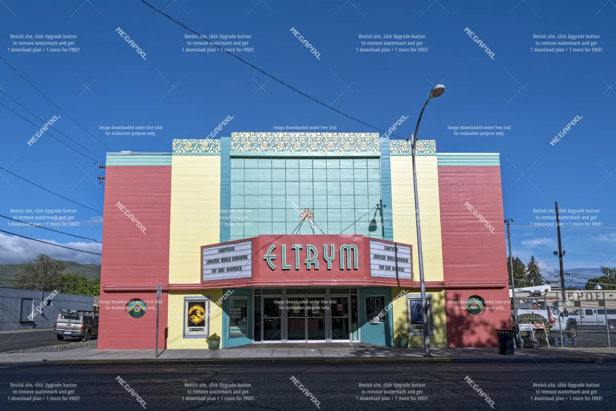 The iconic Eltrym Theater with its art deco marquee and colorful facade, standing as a cultural landmark in downtown Baker City. The energetic scene hints at local performances and social gatherings.