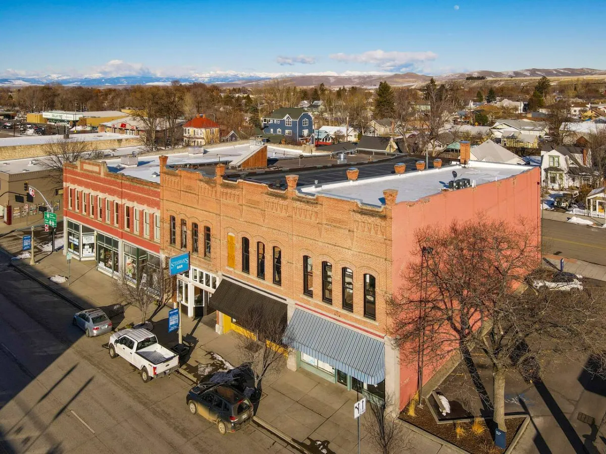 A vibrant downtown street scene with historic brick architecture, colorful storefronts, and a tree-lined avenue bustling with activity. The image suggests easy access to shops, dining, and community events.
